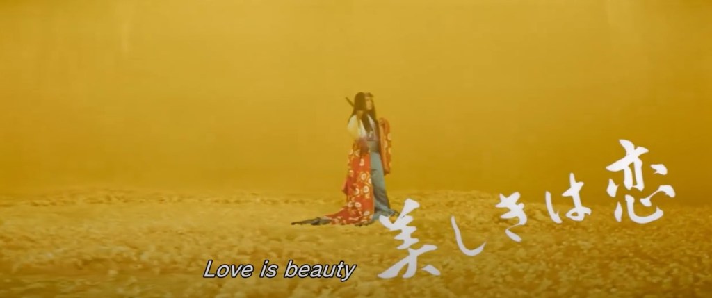 screenshot from The Mad Fox, text reads Love is beauty; Yasuna is in a field of yellow flowers wearing Sakaki's clothes